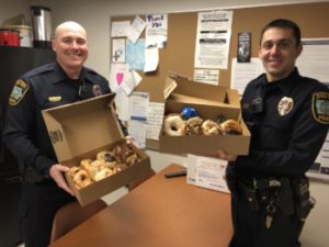 Two Iowa City police officers in uniform displaying boxes of donuts.
