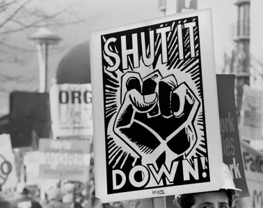 A protest sign that says Shut It Down! It has an image of a fist.