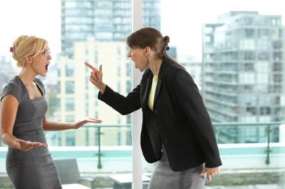 Photo of two women arguing in a white-collar workplace.