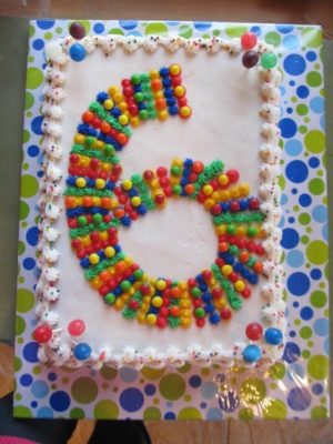A white birthday cake with the number six spelled out in colorful, red, blue, yellow, orange, and green dots.