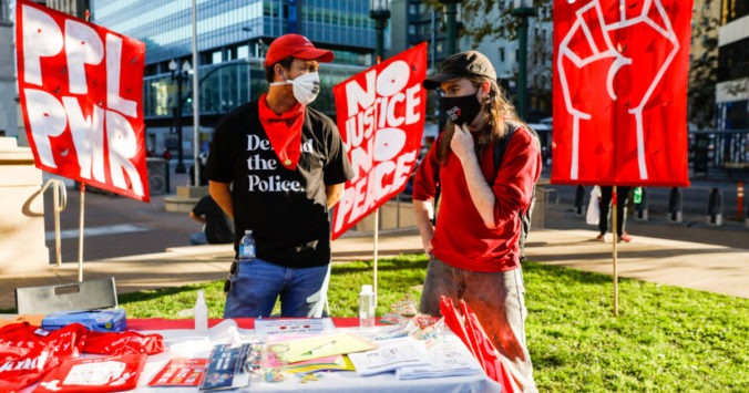 An image of two members of DSA having a discussion in front of protest signs.