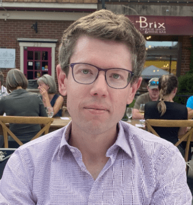 A photo of Matt L. Drabek, a philosophical counselor who is a white man in his late 30s or early 40s. He is wearing stylish glasses and a button up shirt.