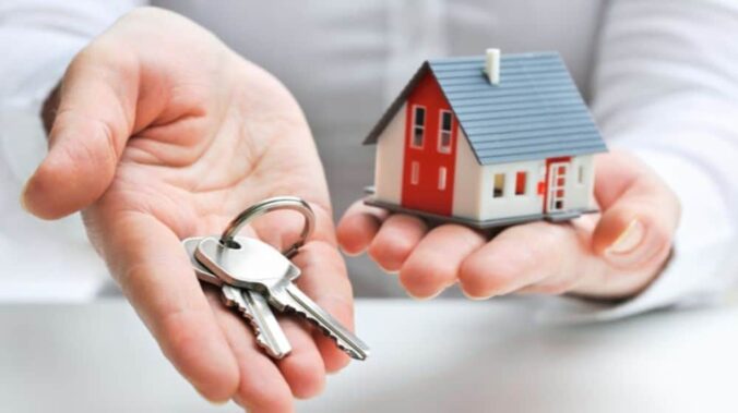 This is a photo of a hand holding a set of keys and another hand holding a small model of a house.