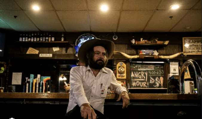 A photo of Iowa Democrat Jon Green sitting in a bar wearing a cowboy hat and a beard.